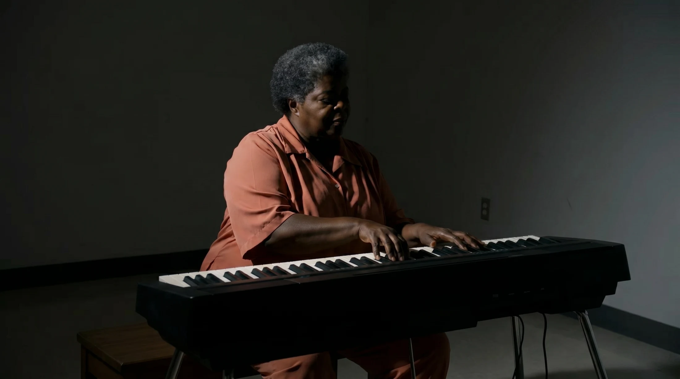 Woman playing an electronic keyboard in a dark room with a narrow chiaroscuro key light