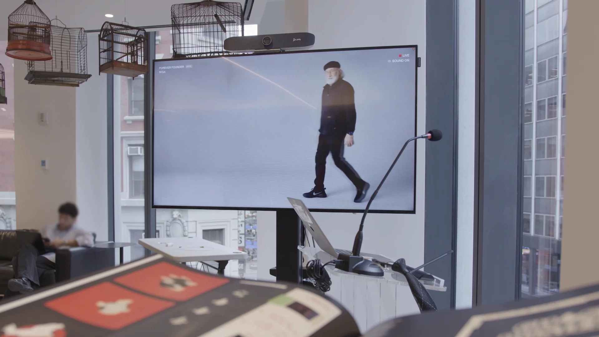 R/GA's full-body Forever Founder AI avatar displayed beside the event microphone and control laptop
