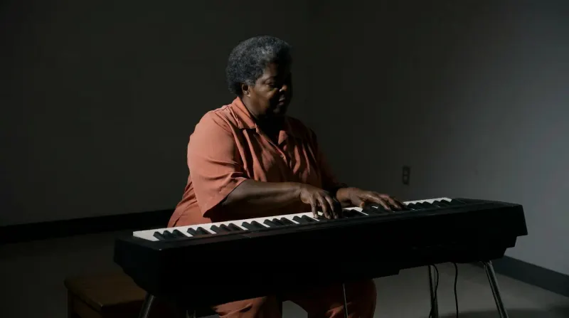 Woman playing an electronic keyboard in a dark room with a narrow chiaroscuro key light